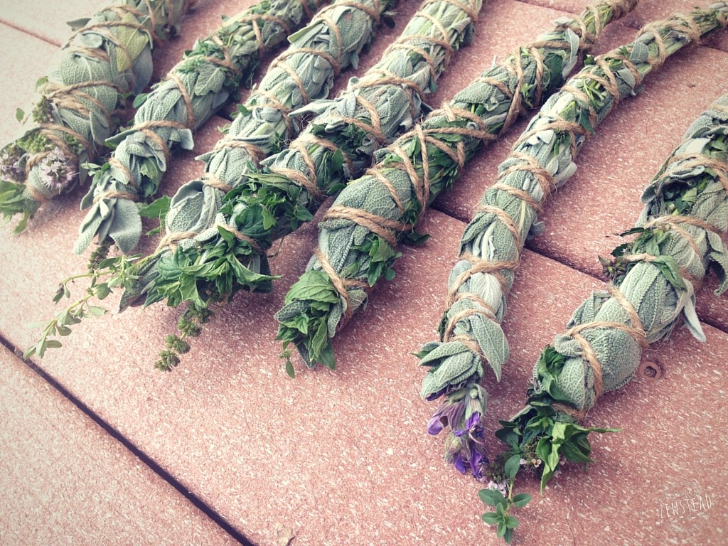 Close up of fresh herbs bound into smudge sticks, laying on a wood deck.