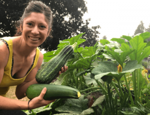 Woman holding two large zucchinis in front of zucchini plant