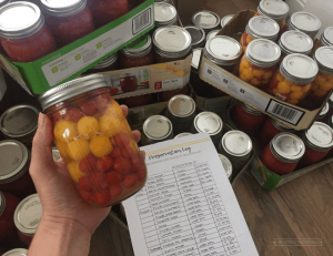 hand holding a jar of canned tomatoes in front of a bunch of stacked cans and a paper that says "Preservation Log"