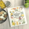 A white binder site on a pale wood background surrounded by an egg basket, a green plant and two glass jars of canned food. The cover of the binder shows images of farm scenes and has the title: 2022 Homestead Management Binder