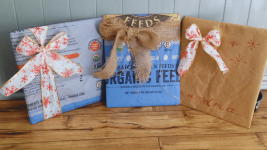 Three presents sit on a wood floor. The presents are wrapped in feed bags and tied with Christmas ribbon