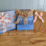 Three presents sit on a wood floor. The presents are wrapped in feed bags and tied with Christmas ribbon