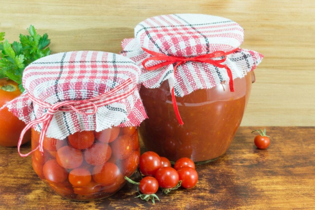 A jar of canned cherry tomatoes with their skins on, and a jar of tomato sauce